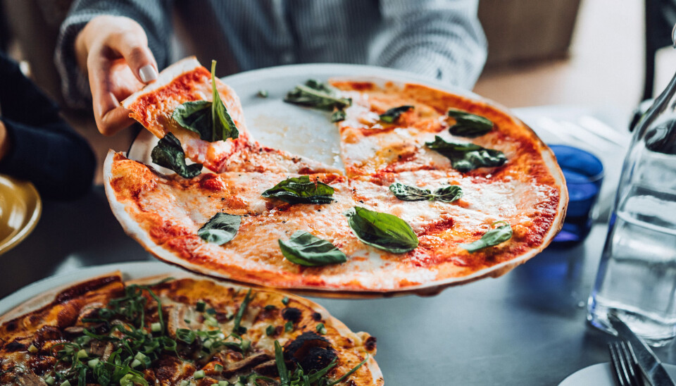En person tager et stykke af en margaritha pizza på en restaurant.